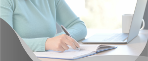 agenda de exames - mulher utilizando blusa azul escrevendo em uma agenda de papel com uma caneta preta